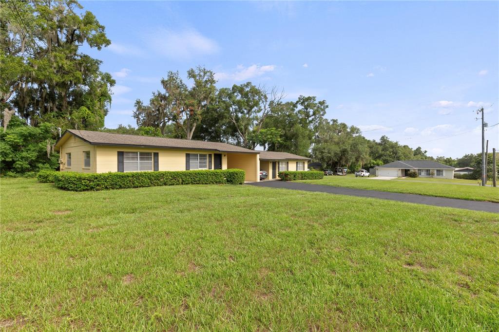 A yellow, single-story duplex with a long driveway sits on a grassy lot — 12215 LEANNE DRIVE, DADE CITY, FL