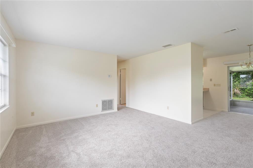 An empty living room features beige walls, gray carpeting, and a sliding glass door — 12215 LEANNE DRIVE, DADE CITY, FL