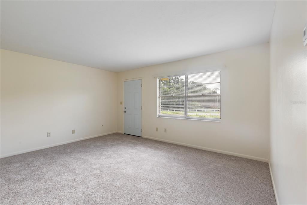 An empty room features beige walls, gray carpeting, a window with blinds, and a door — 12215 LEANNE DRIVE, DADE CITY, FL