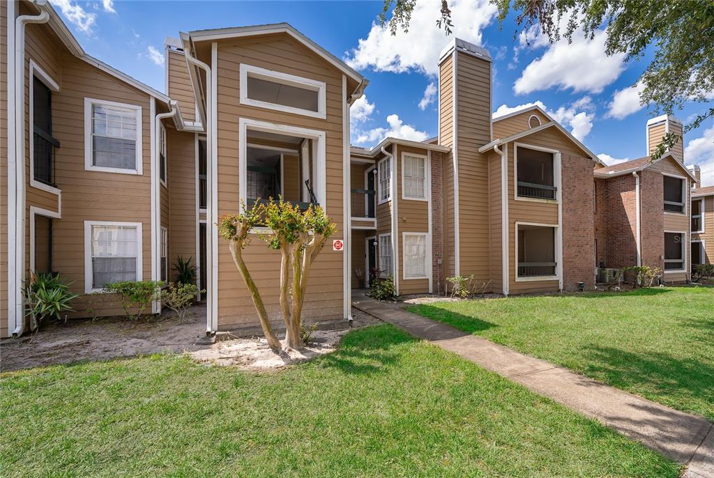 A two-story apartment building with tan siding, brick accents, and a concrete walkway — 4367 THORNBRIAR LANE UNIT 206, ORLANDO, FL