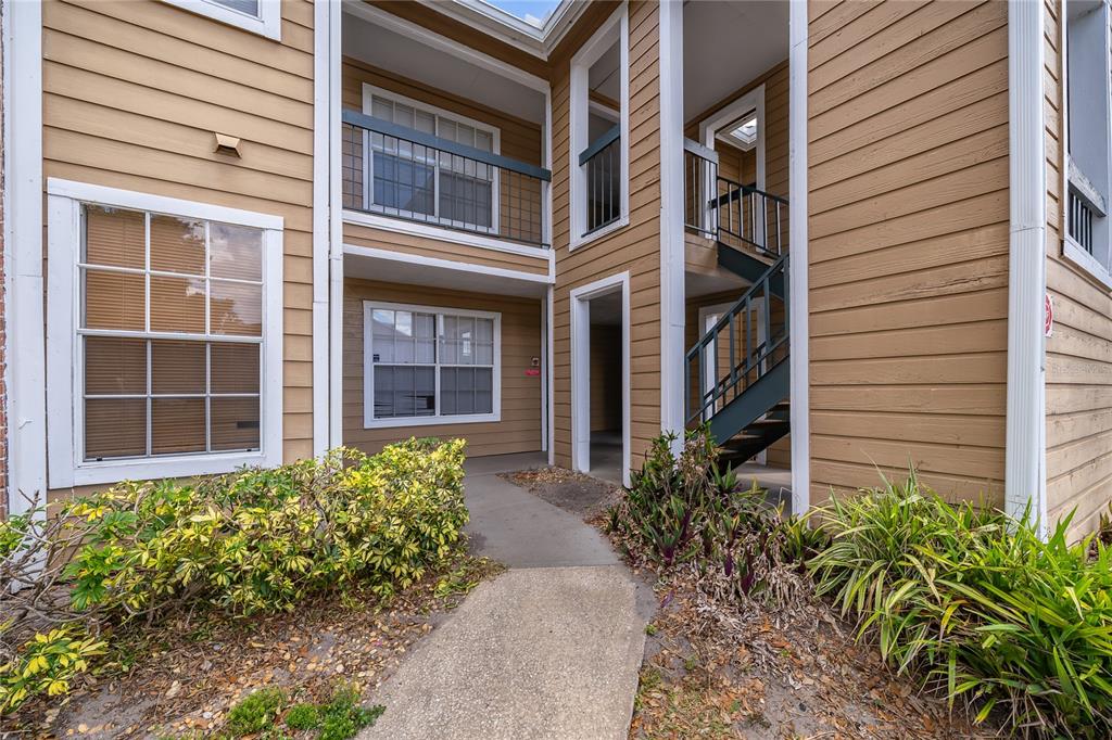 An exterior view of a two-story apartment building with tan siding and a concrete walkway — 4367 THORNBRIAR LANE UNIT 206, ORLANDO, FL