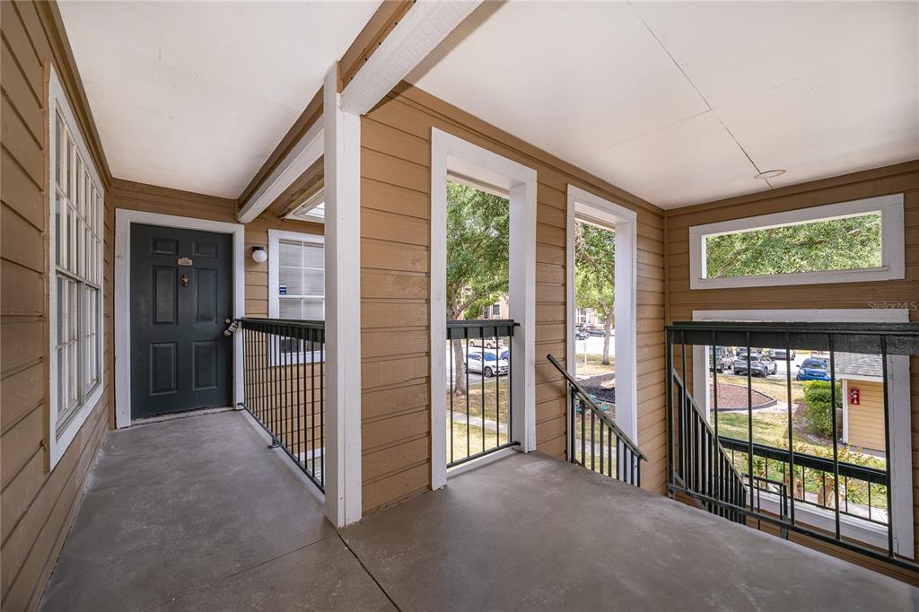 An outdoor covered walkway with a dark door, metal railings, and stairs leading down — 4367 THORNBRIAR LANE UNIT 206, ORLANDO, FL