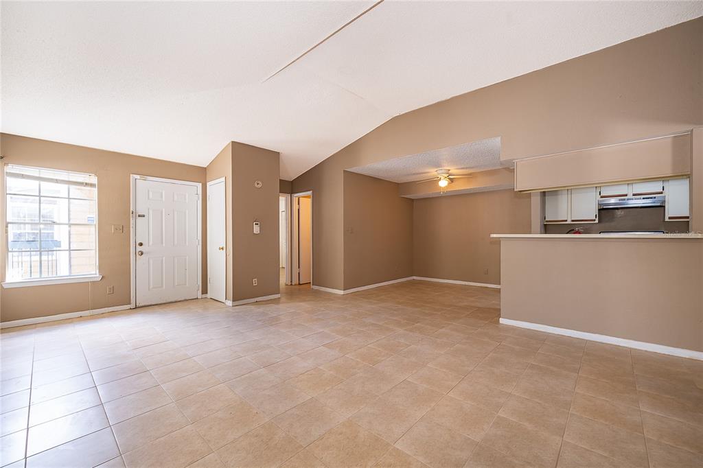 A living room with beige tile flooring, vaulted ceilings, and an open kitchen pass-through — 4367 THORNBRIAR LANE UNIT 206, ORLANDO, FL