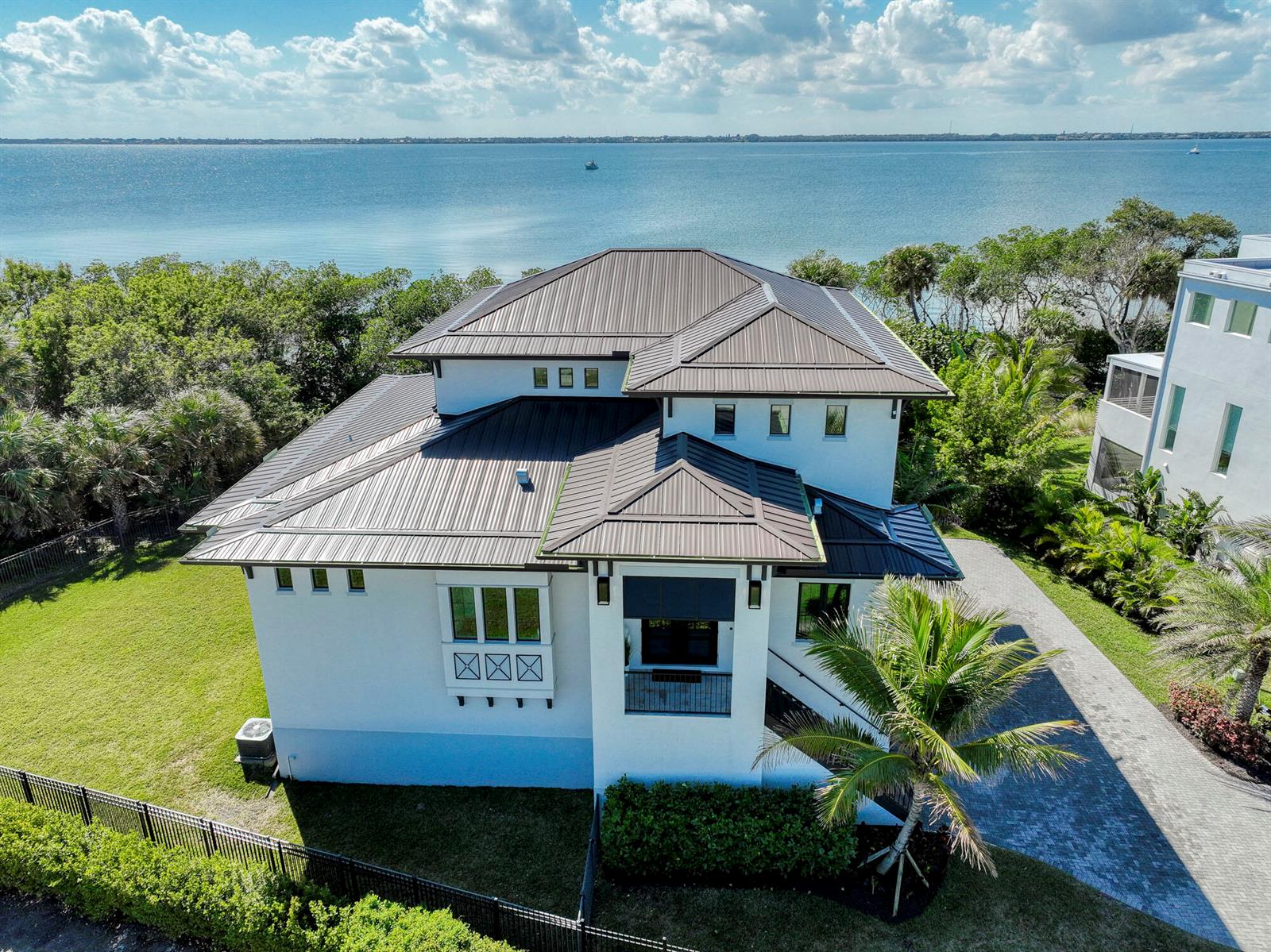 An aerial view of a white multi-story house with a dark metal roof near water — 7683 Pelican Pointe Drive, Jensen Beach FL 34957, JENSEN BEACH, FL