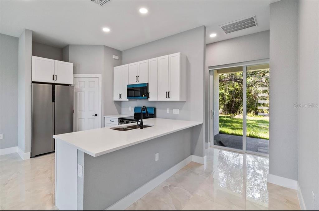 A modern kitchen features white cabinets, stainless steel appliances, a quartz island, and sliding doors — 20462 KENILWORTH BOULEVARD, PORT CHARLOTTE, FL