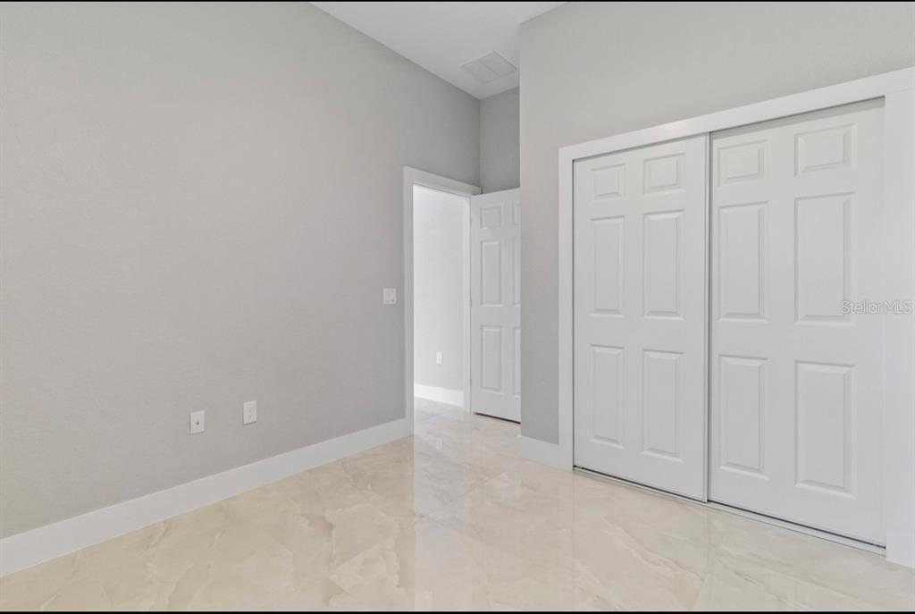 An empty room features light gray walls, white trim, sliding closet doors, and polished tile flooring — 20462 KENILWORTH BOULEVARD, PORT CHARLOTTE, FL