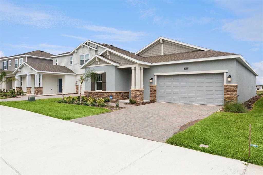 A single-story house with a gray stucco exterior, stone accents, and a paved driveway — 3012 NAMASTE DRIVE, CLERMONT, FL