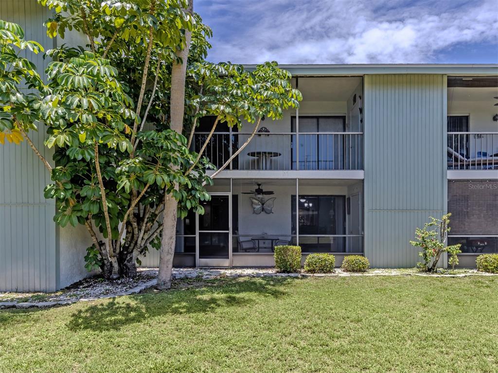 A two-story apartment building exterior features a ground-floor screened patio and an upper-level balcony — 1730 MANASOTA BEACH ROAD UNIT 107, ENGLEWOOD, FL