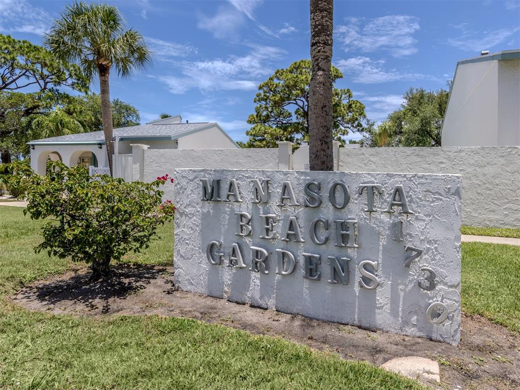 A stone sign for Manasota Beach Gardens stands in a grassy area with palm trees — 1730 MANASOTA BEACH ROAD UNIT 107, ENGLEWOOD, FL