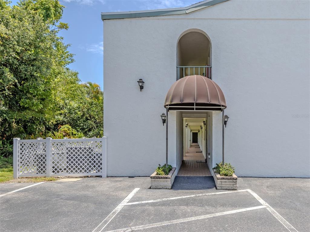 An exterior view of a white building with a brown awning over a covered walkway — 1730 MANASOTA BEACH ROAD UNIT 107, ENGLEWOOD, FL