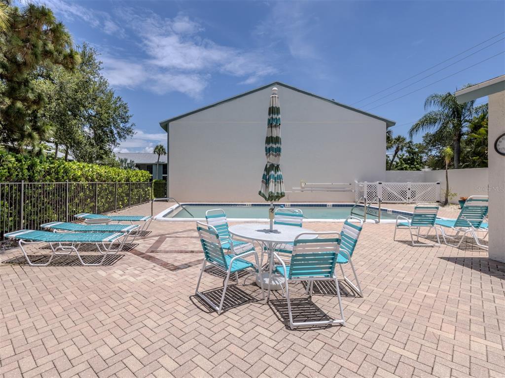 A patio with a dining set and lounge chairs sits beside a rectangular swimming pool — 1730 MANASOTA BEACH ROAD UNIT 107, ENGLEWOOD, FL