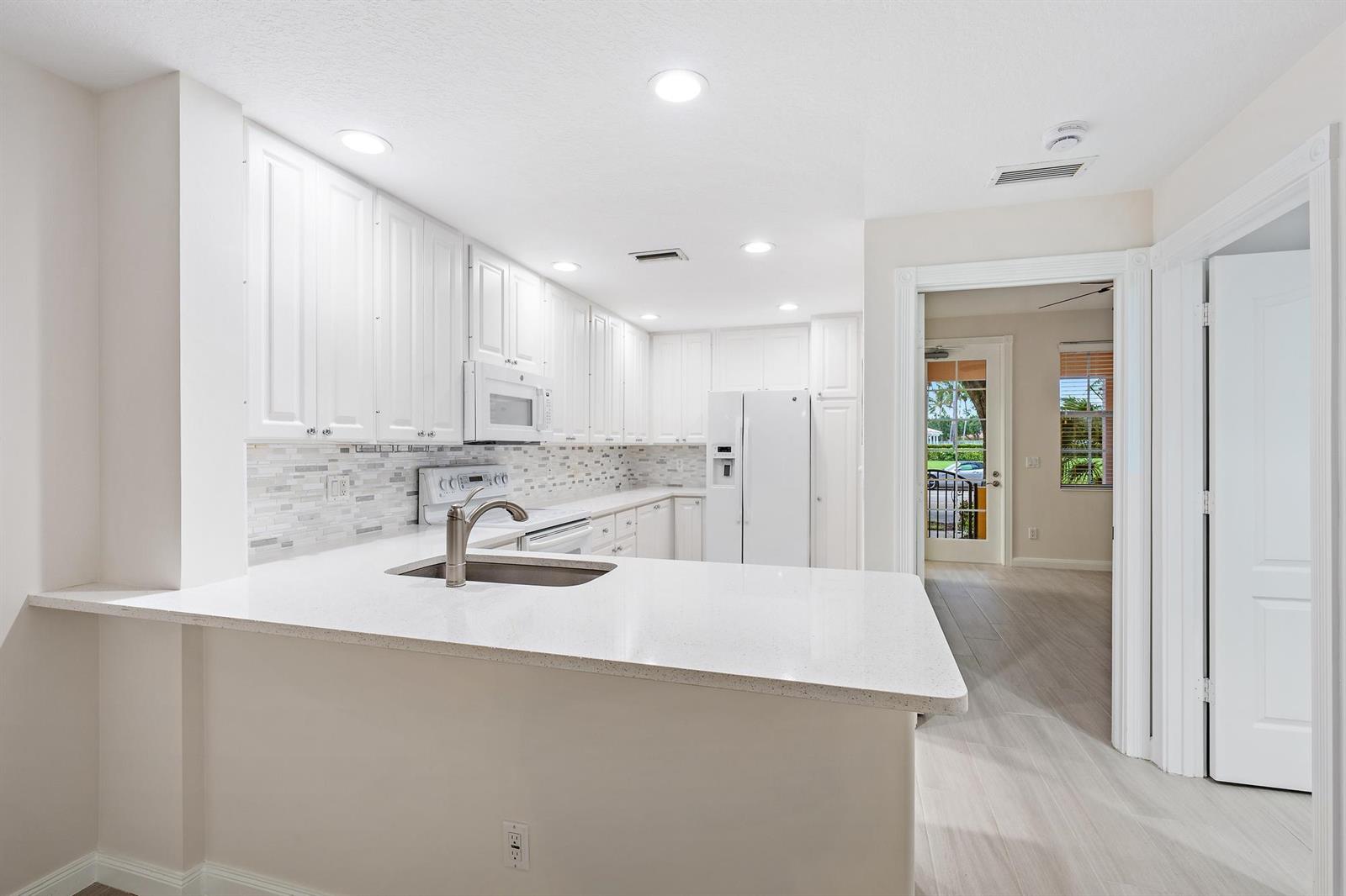 A white kitchen features quartz countertops, white cabinetry, a tile backsplash, and a breakfast bar — 1856 Jeaga Drive, Jupiter FL 33458, JUPITER, FL