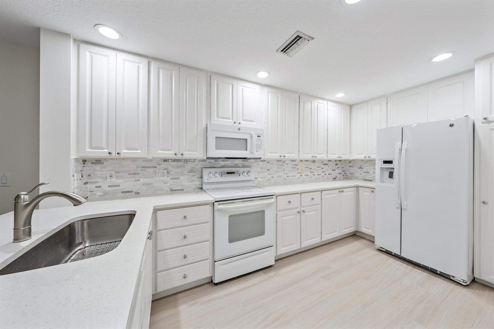 A kitchen features white cabinets, stainless steel sink, white appliances, and a tiled backsplash — 1856 Jeaga Drive, Jupiter FL 33458, JUPITER, FL