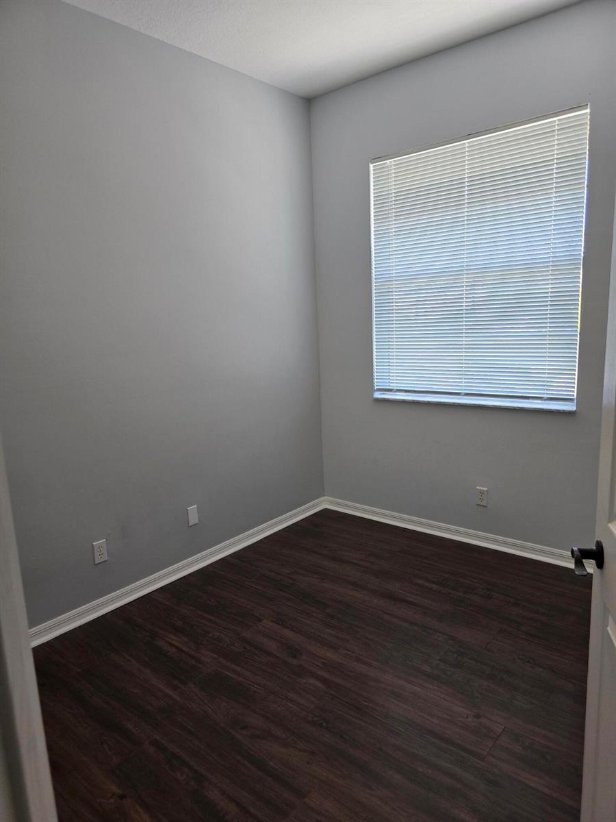 An empty room with gray walls, dark wood-look flooring, and a window with white blinds — 4261 E Main Street E, Jupiter FL 33458, JUPITER, FL