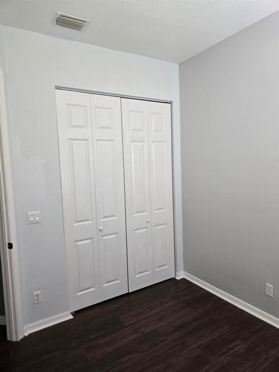 A room with light gray walls, dark wood-look flooring, and white bi-fold closet doors — 4261 E Main Street E, Jupiter FL 33458, JUPITER, FL