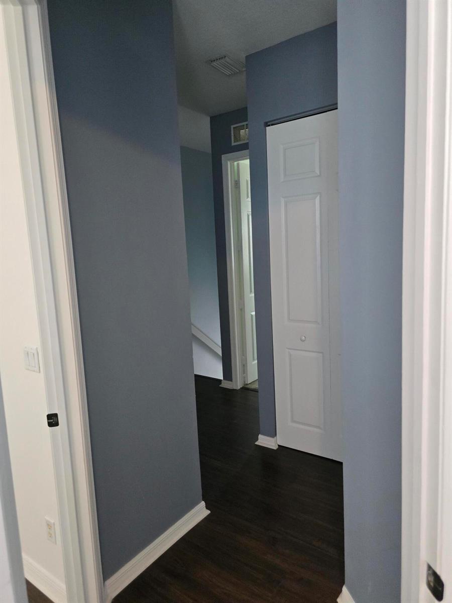 A hallway with blue walls, dark wood flooring, and white trim leads to a doorway — 4261 E Main Street E, Jupiter FL 33458, JUPITER, FL