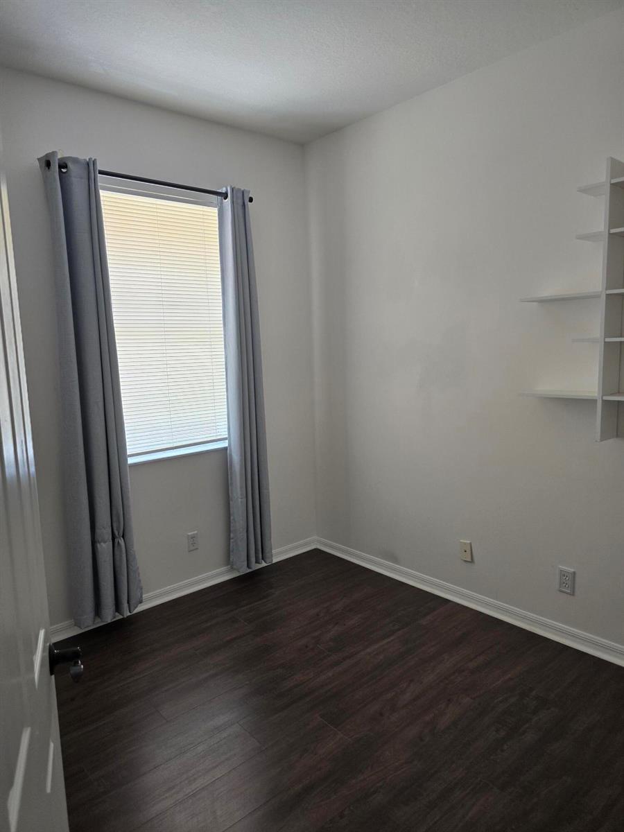 A small room features dark wood-look flooring, light gray walls, a window with curtains, and wall-mounted shelves — 4261 E Main Street E, Jupiter FL 33458, JUPITER, FL