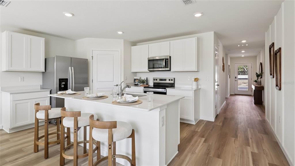 A modern kitchen features white cabinetry, a central island with bar stools, and wood flooring — 11008 NW 167TH TERRACE, ALACHUA, FL