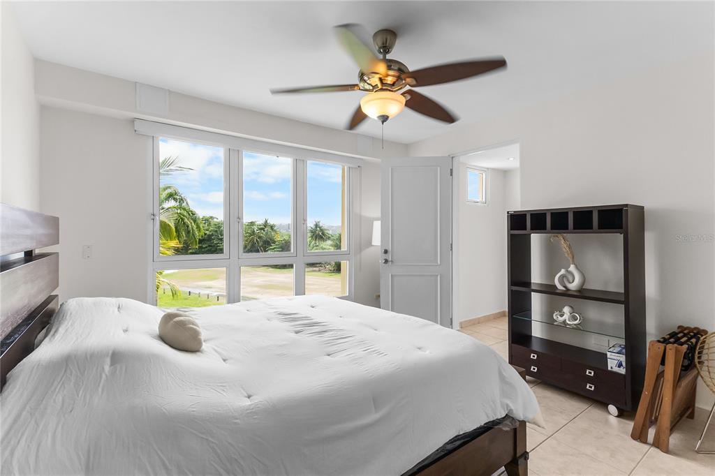 A bedroom features a bed, a ceiling fan, a bookshelf, and large windows with outdoor views — 500 OCEAN DRIVE UNIT 535, HUMACAO, PR