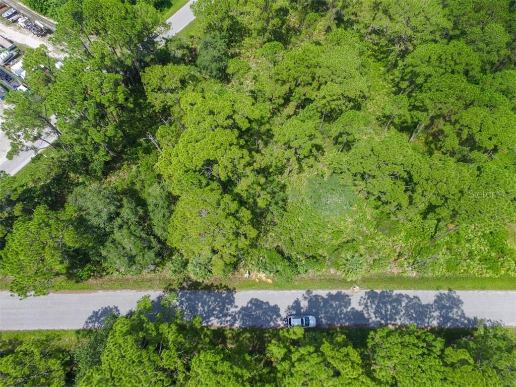 An aerial view shows a wooded lot bordering a paved road with a parked car — LOTS 15,16,17 TEGASTAS STREET, NORTH PORT, FL