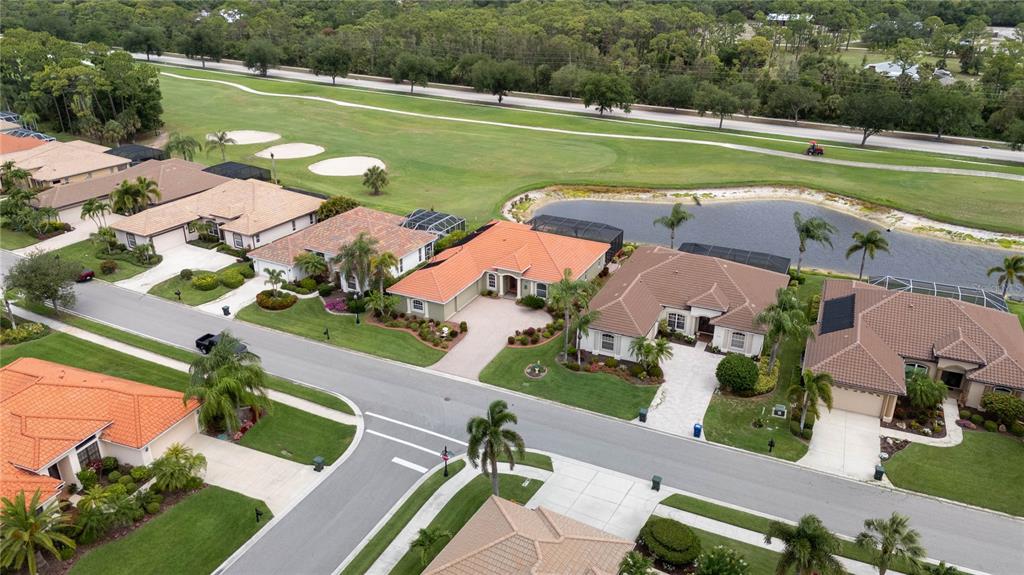An aerial view shows a suburban neighborhood with houses, a pond, and a golf course — 1038 TUSCANY BOULEVARD, VENICE, FL