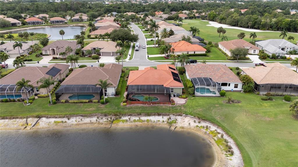 An aerial view shows a row of houses with swimming pools bordering a small lake — 1038 TUSCANY BOULEVARD, VENICE, FL