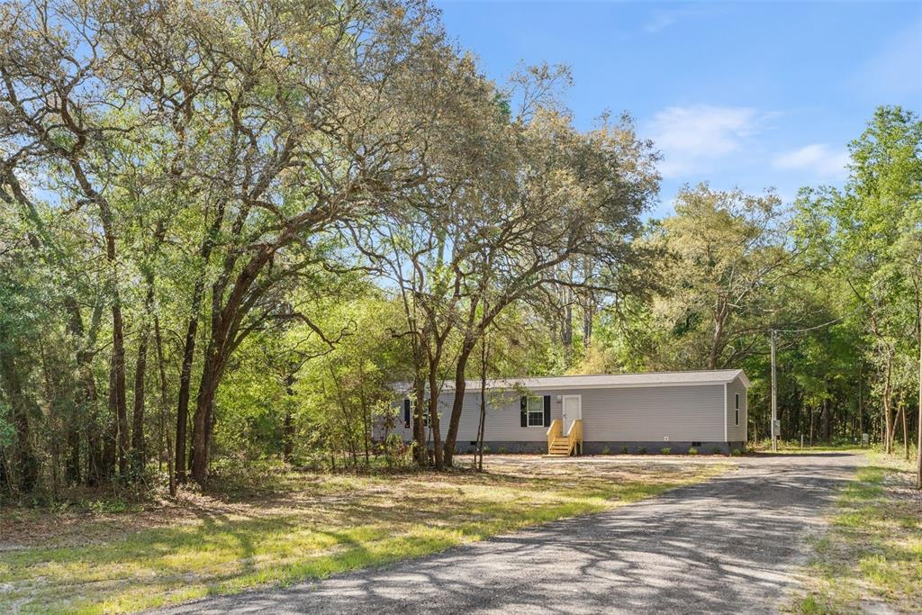 A single-story manufactured home sits on a wooded lot with a gravel driveway — 10970 NE 71ST STREET, BRONSON, FL