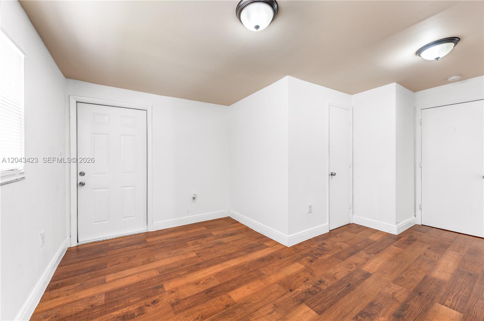 An empty room features white walls, wood-look flooring, two ceiling lights, and three white doors — 8057 NE 1st Ave # 2, Miami FL 33138, MIAMI, FL