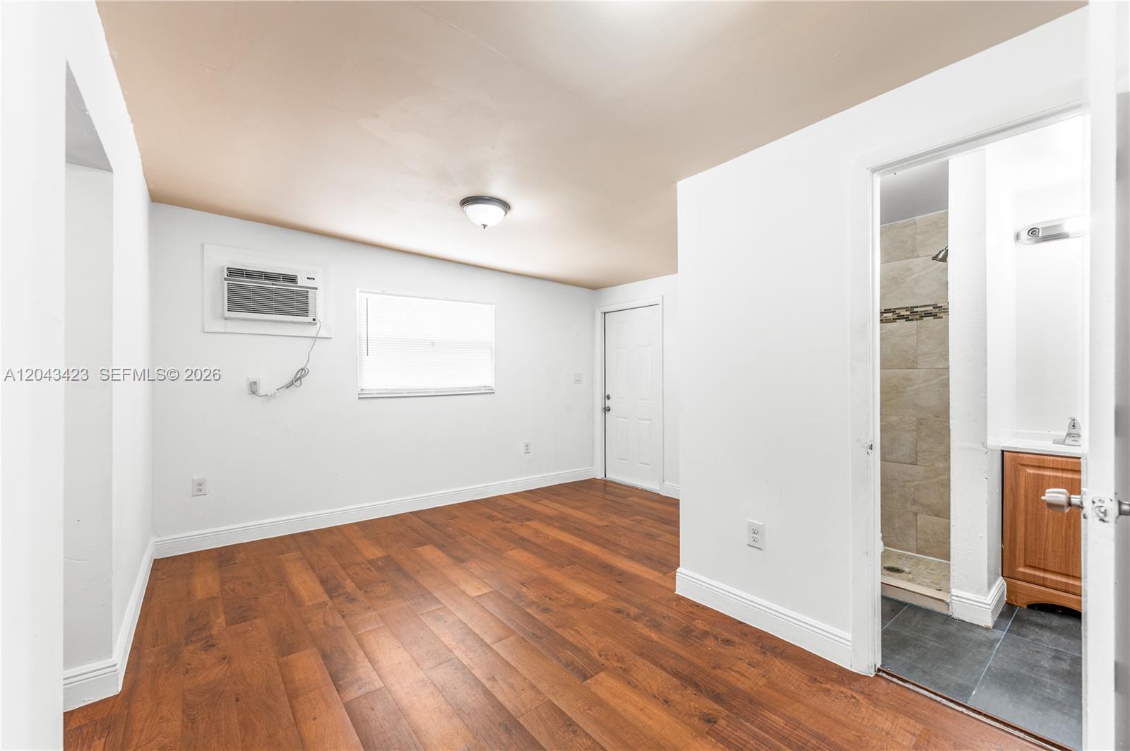 An empty room with wood-look flooring, a window air conditioner, and an attached bathroom — 8057 NE 1st Ave # 2, Miami FL 33138, MIAMI, FL