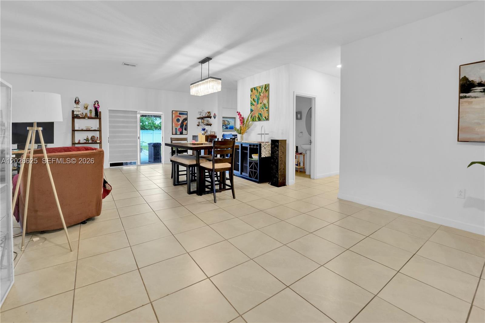 A bright, open-concept living and dining area features light tile flooring and a sliding glass door — 21460 SW 127th Pl, Miami FL 33177, MIAMI, FL