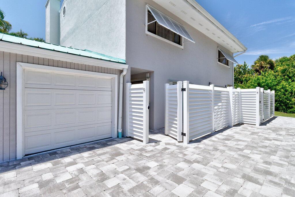 A white garage door and louvered privacy fence stand beside a gray two-story house — VERO BEACH, FL