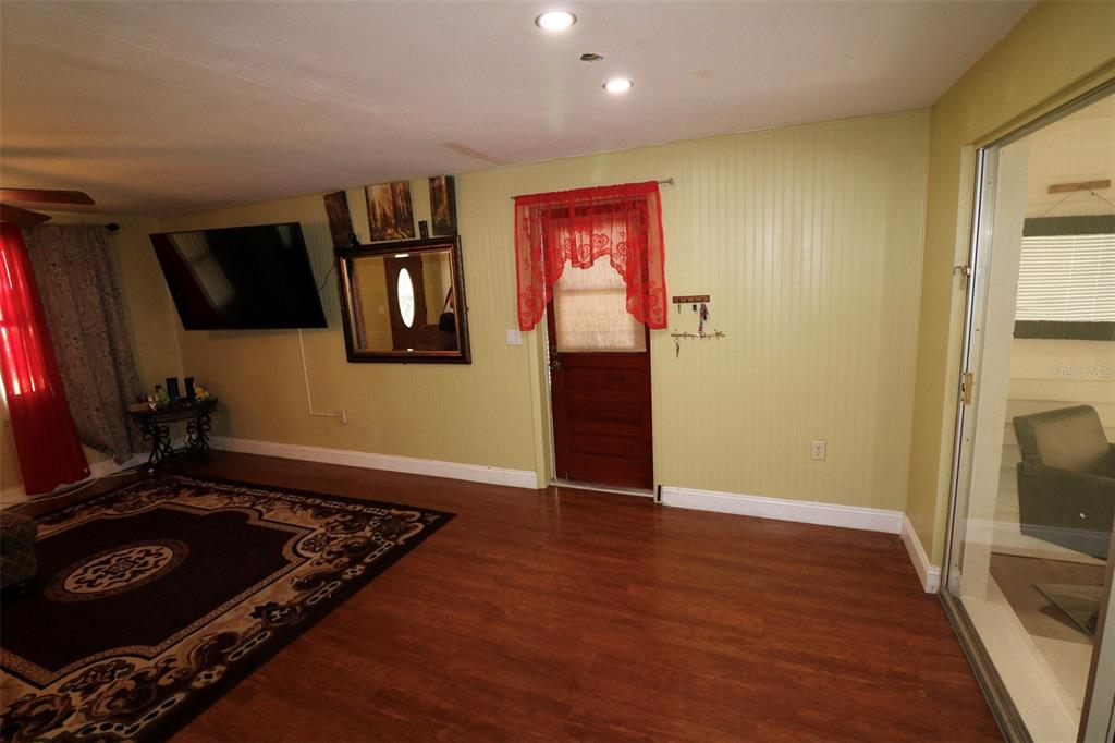 A living room features wood-look flooring, light green walls, a television, and a red-curtained door — 3022 VENICE WAY, LAKELAND, FL