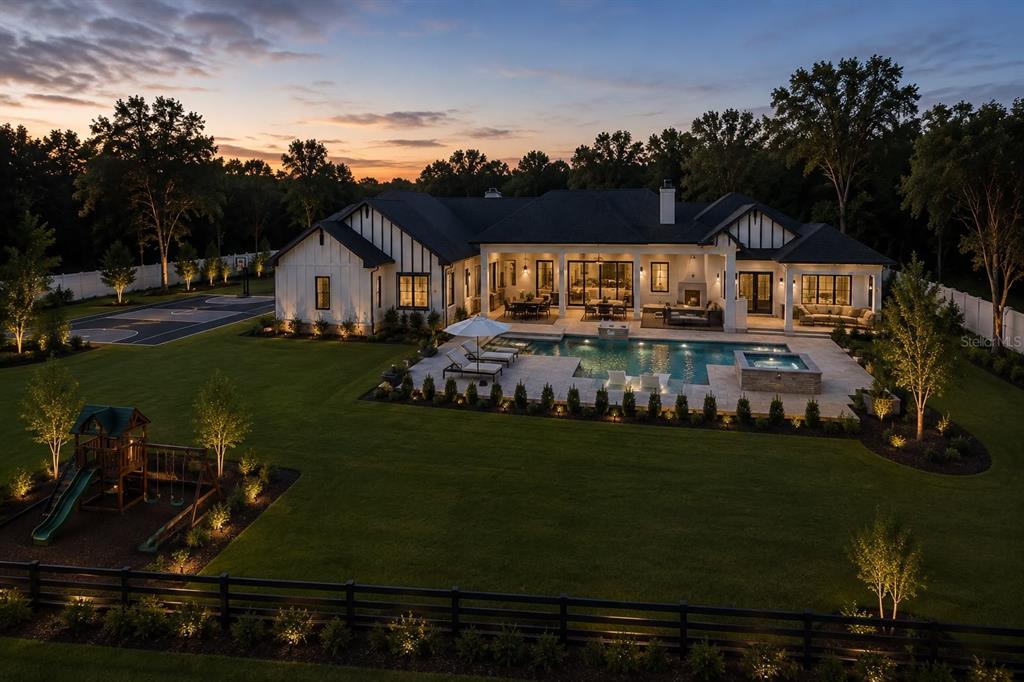 A modern farmhouse with a pool, hot tub, basketball court, and playground at sunset — 10623 LITHIA ESTATES DRIVE, LITHIA, FL