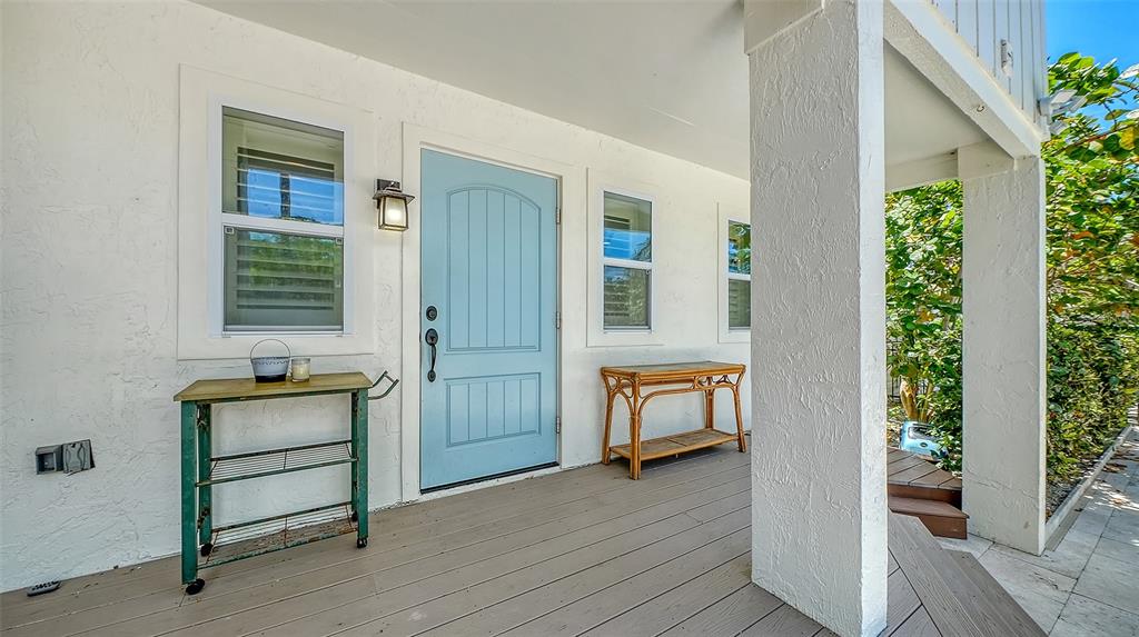 A light blue front door sits on a covered porch with a metal cart and table — 3708 SANDSPUR LANE, NOKOMIS, FL