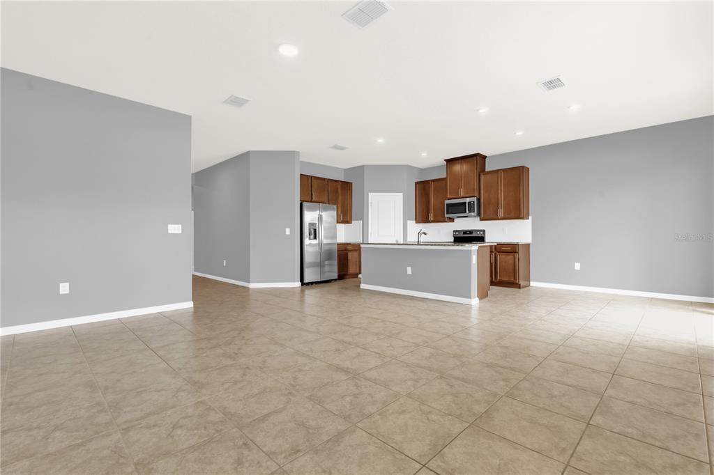 A kitchen with brown cabinets, stainless steel appliances, and a central island on tile flooring — 29307 MEADOWCROFT AVENUE, WESLEY CHAPEL, FL