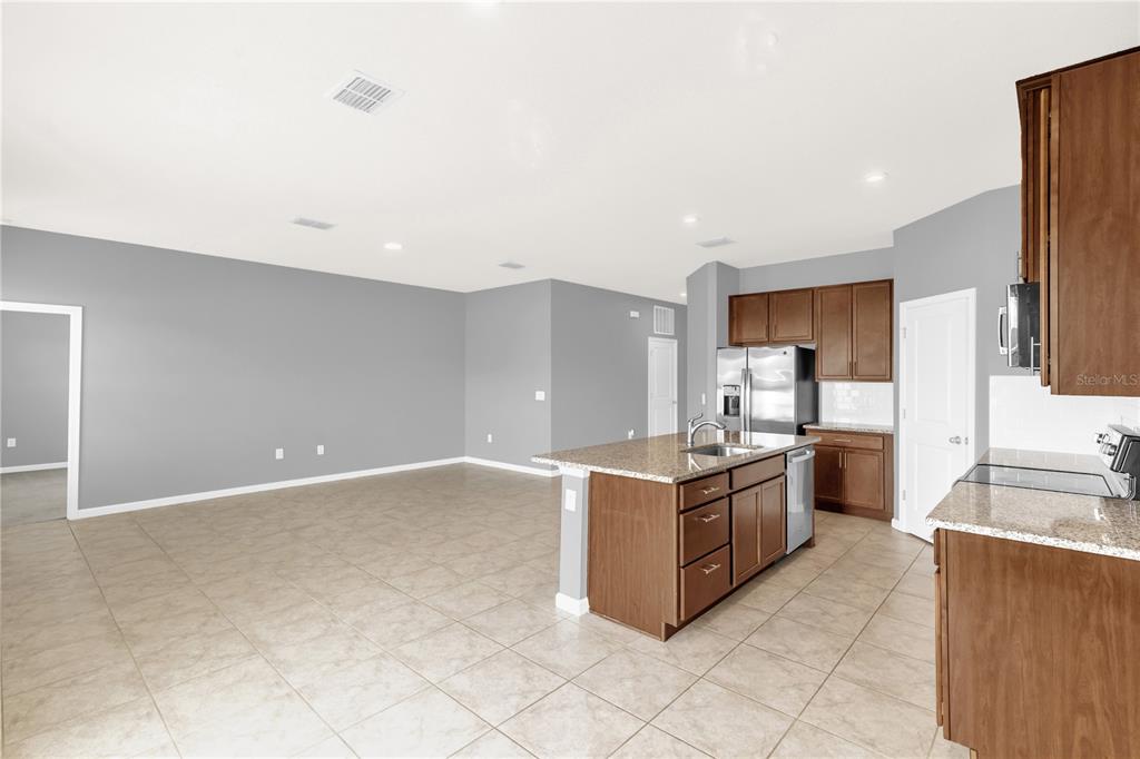 A kitchen with wood cabinets and granite countertops opens into a large, tiled living area — 29307 MEADOWCROFT AVENUE, WESLEY CHAPEL, FL