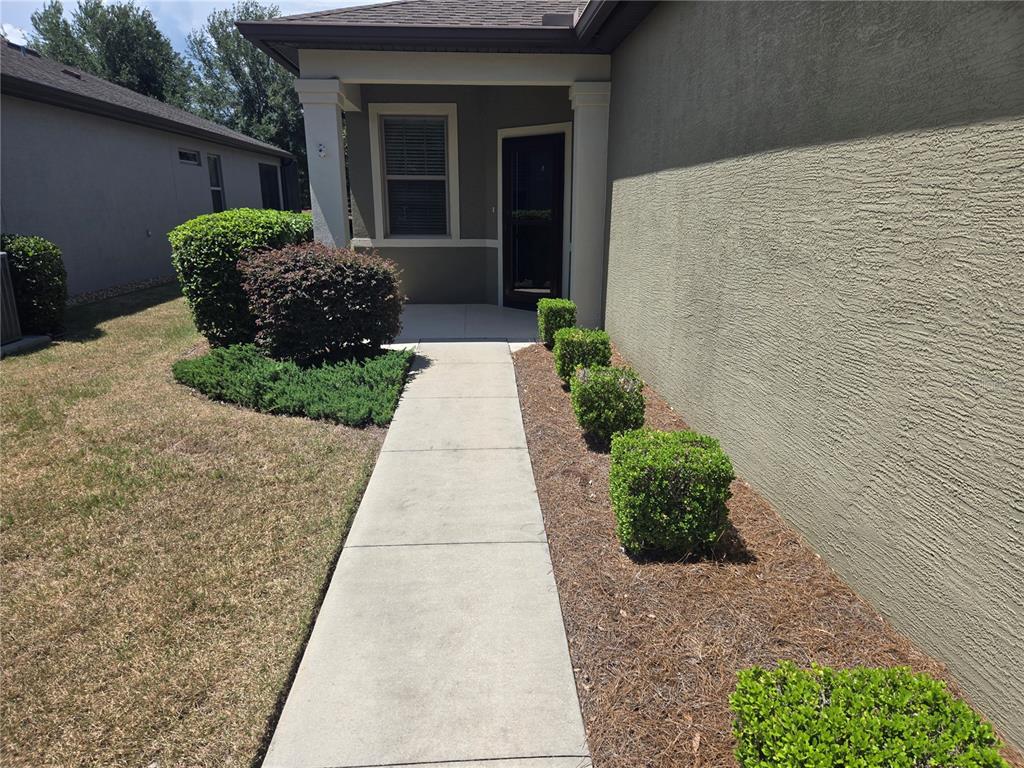 A concrete walkway leads to the front entrance of a house with stucco siding — 7692 SW 94TH CIRCLE, OCALA, FL