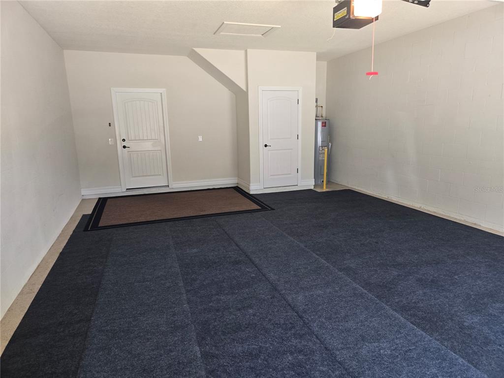A garage with a gray carpeted floor, two white doors, and a water heater — 7692 SW 94TH CIRCLE, OCALA, FL