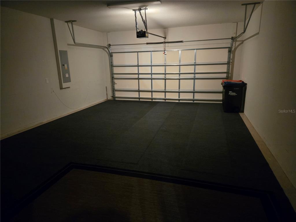 A garage with white walls, a metal door, and dark rubber flooring mats — 7692 SW 94TH CIRCLE, OCALA, FL