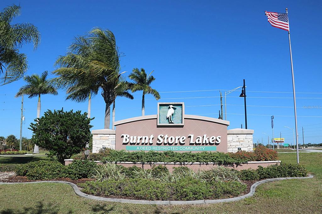 A sign for Burnt Store Lakes stands in a landscaped area under a clear blue sky — 17503 MALARKY LANE, PUNTA GORDA, FL