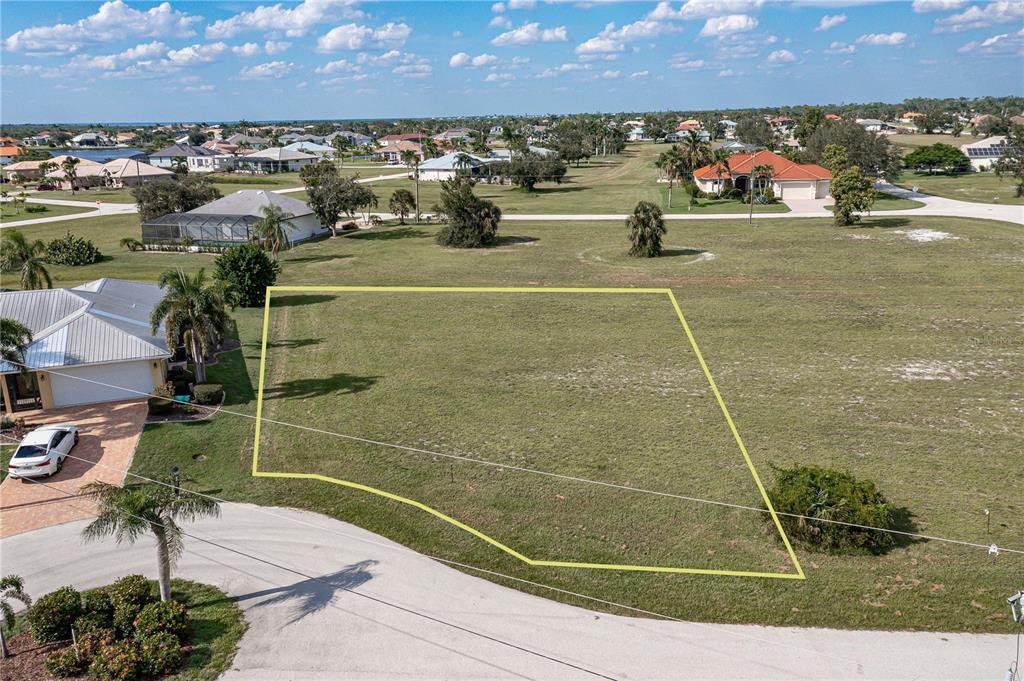 An aerial view shows a vacant residential lot outlined in yellow along a paved road — 17503 MALARKY LANE, PUNTA GORDA, FL
