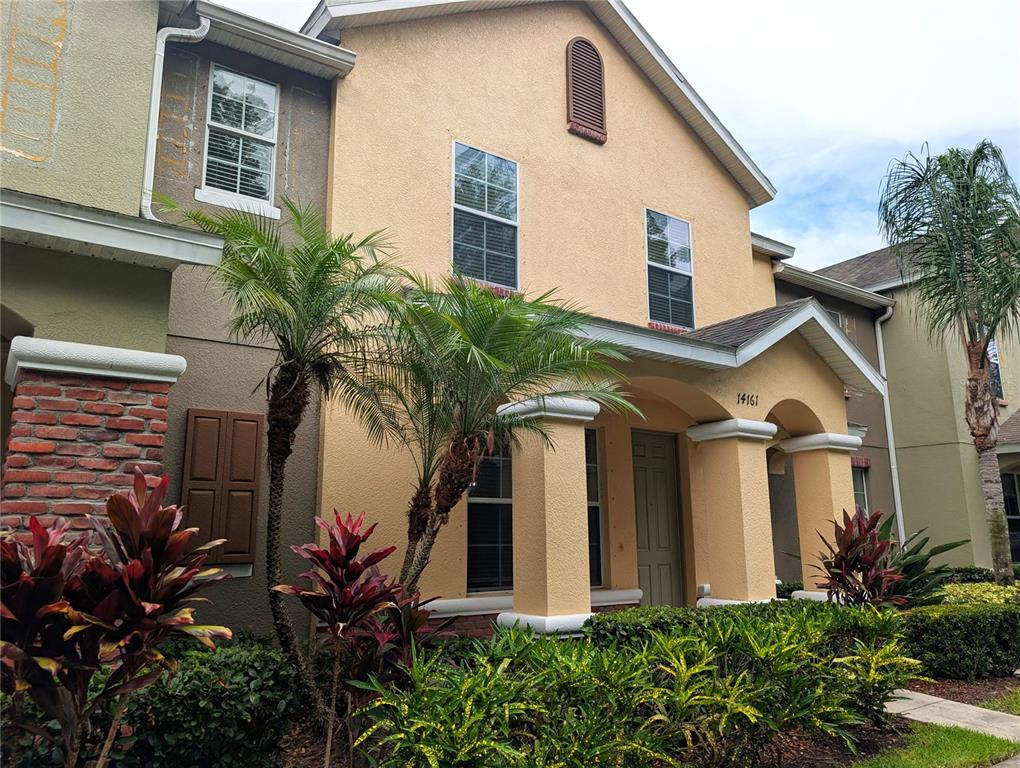 A two-story stucco townhouse features a covered entryway, brick accents, and tropical landscaping — 14161 STOWBRIDGE AVENUE, TAMPA, FL