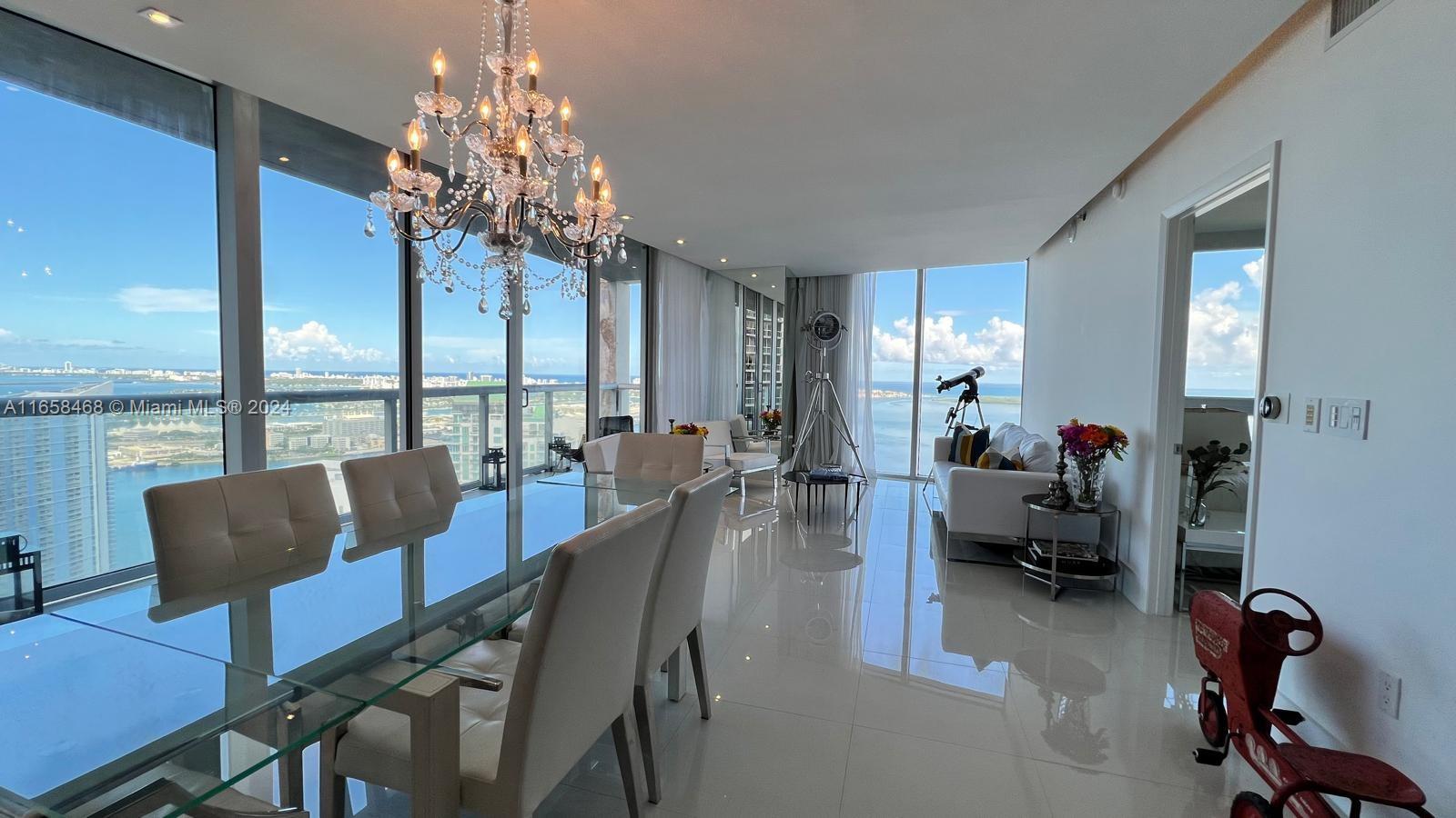 A modern dining and living area features floor-to-ceiling windows, a glass table, and a chandelier — 495 Brickell Ave # 4902, Miami FL 33131, MIAMI, FL