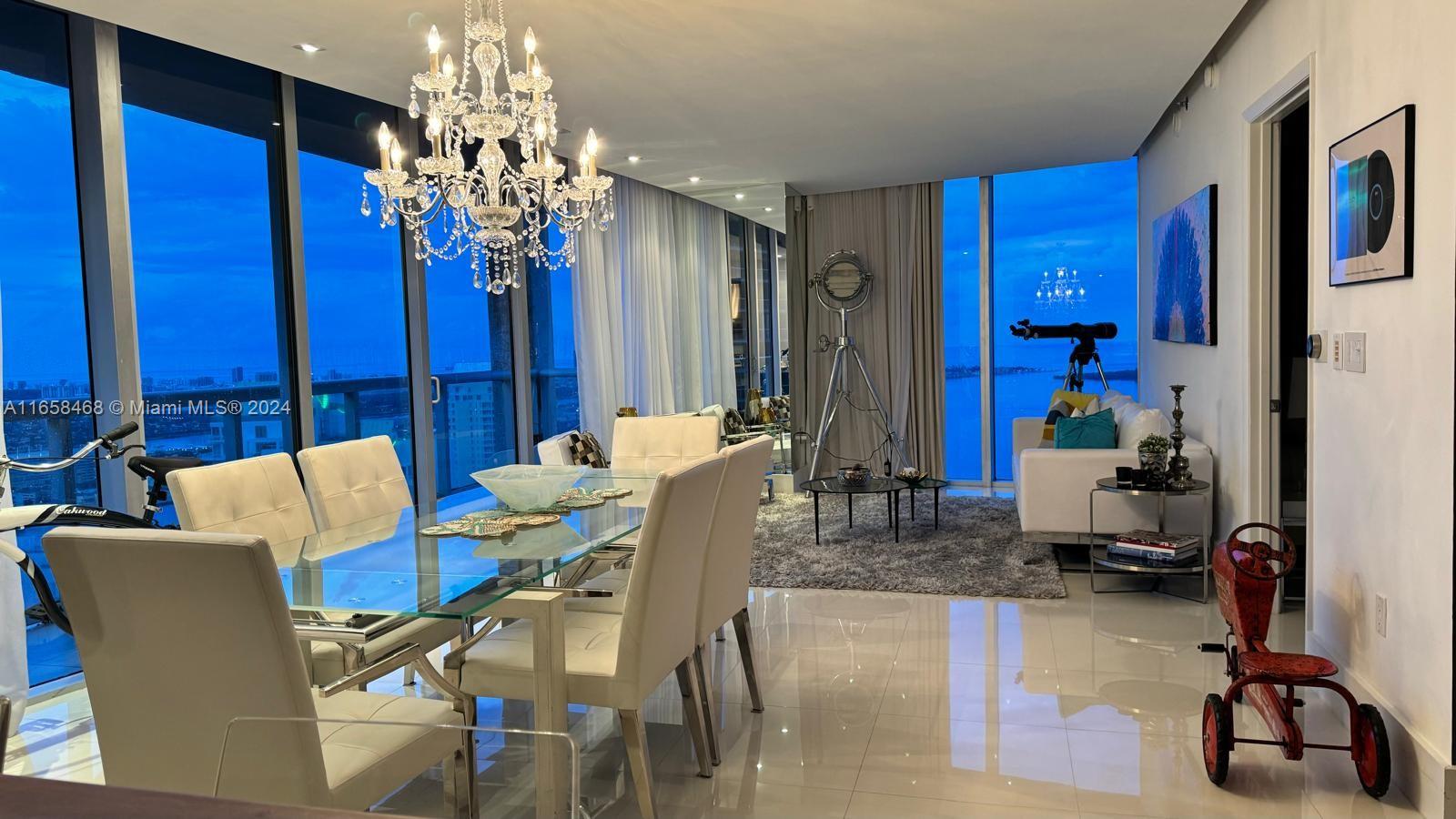 A dining area with a glass table and chandelier opens into a living room with floor-to-ceiling windows — 495 Brickell Ave # 4902, Miami FL 33131, MIAMI, FL