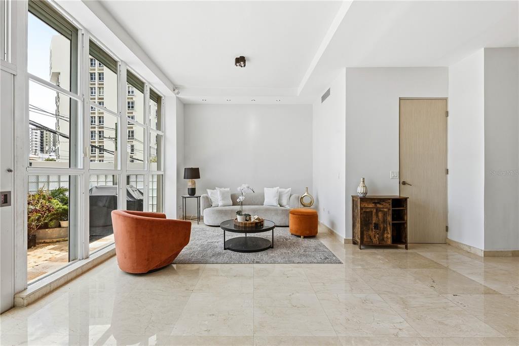 A modern living room features a grey sofa, orange accent chair, and large floor-to-ceiling windows — 1362 MAGDALENA AVENUE UNIT Villa 109, SAN JUAN, PR