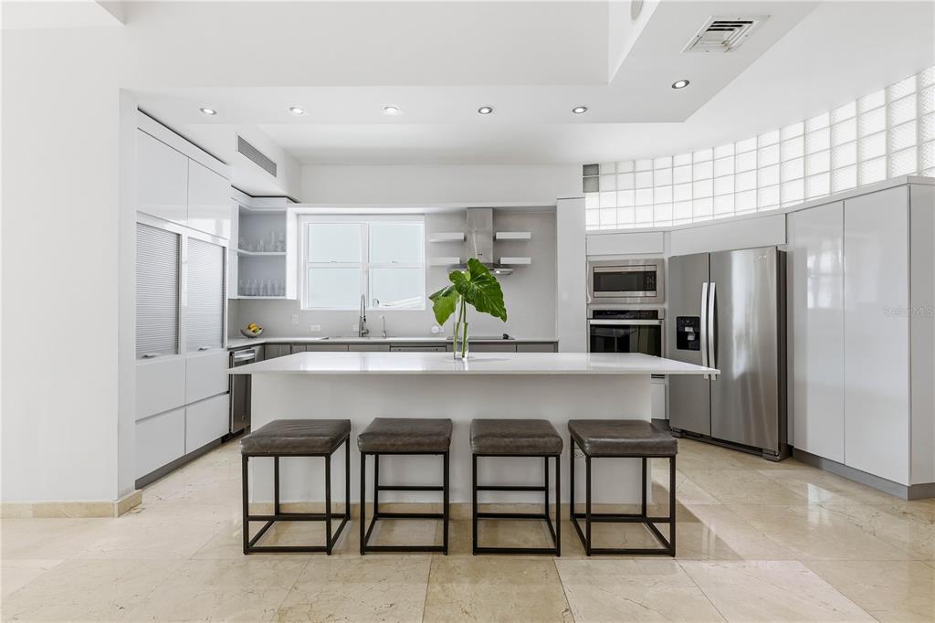 A modern white kitchen features a central island with four stools and stainless steel appliances — 1362 MAGDALENA AVENUE UNIT Villa 109, SAN JUAN, PR