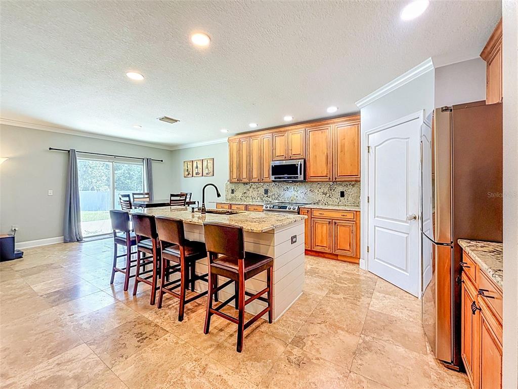 A kitchen features a granite-topped island, wooden cabinetry, stainless steel appliances, and tiled flooring — 420 HARTFORD HEIGHTS STREET, SPRING HILL, FL