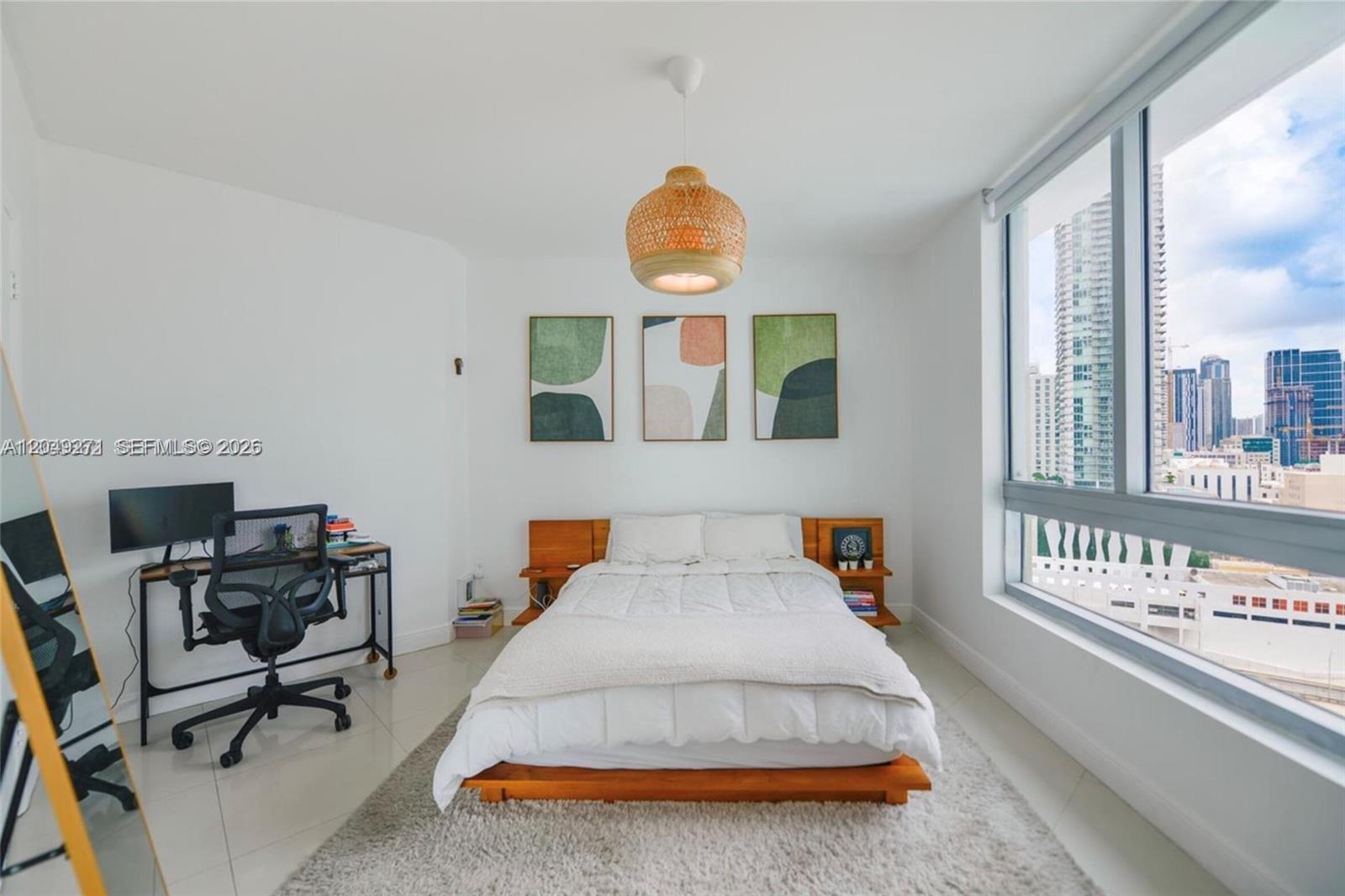 A bedroom features a wooden bed frame, a desk, and a large window with city views — 350 S Miami Ave # 1911, Miami FL 33130, MIAMI, FL
