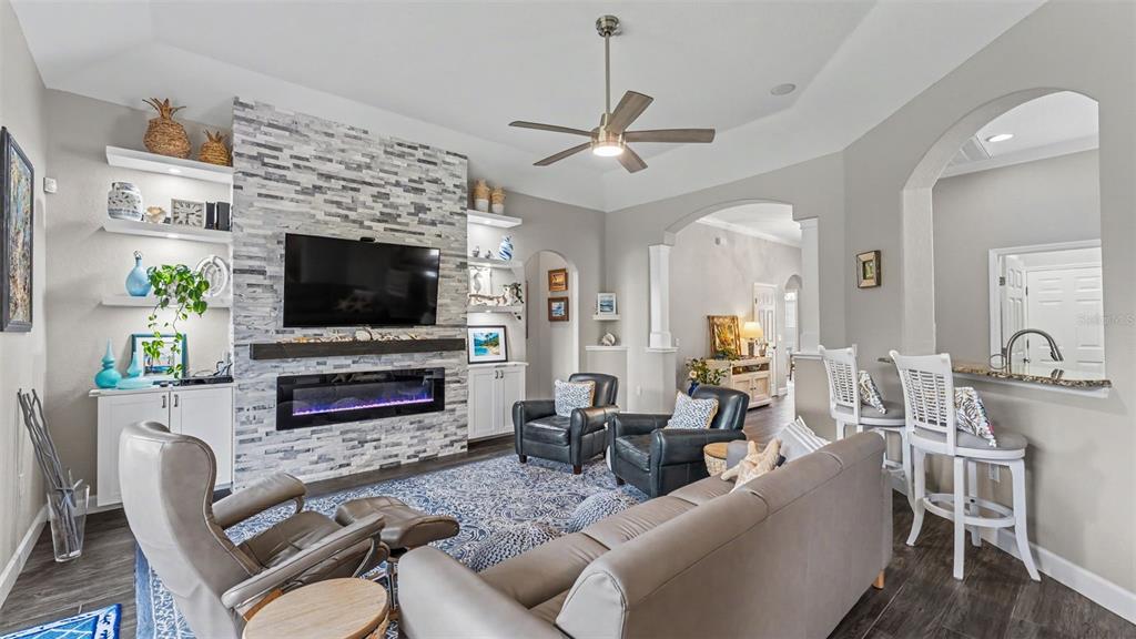 A living room features a stone fireplace, a ceiling fan, and an adjacent breakfast bar — 2775 HIGHLANDS CREEK DRIVE, LAKELAND, FL