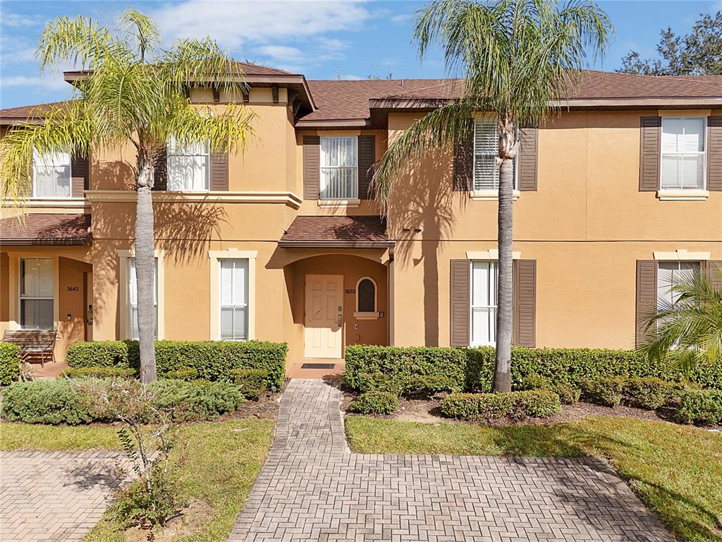 A two-story tan stucco townhouse with a paved walkway and two palm trees in front — 2632 CALABRIA AVENUE, DAVENPORT, FL